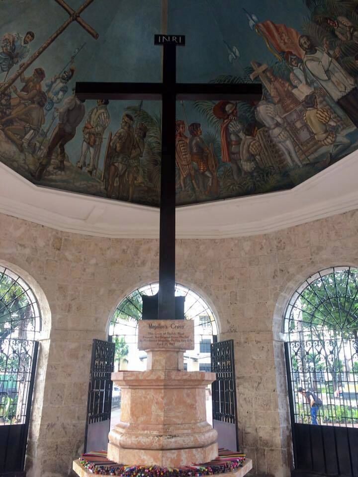 A historical monument with a cross, surrounded by stone walls and arched windows.