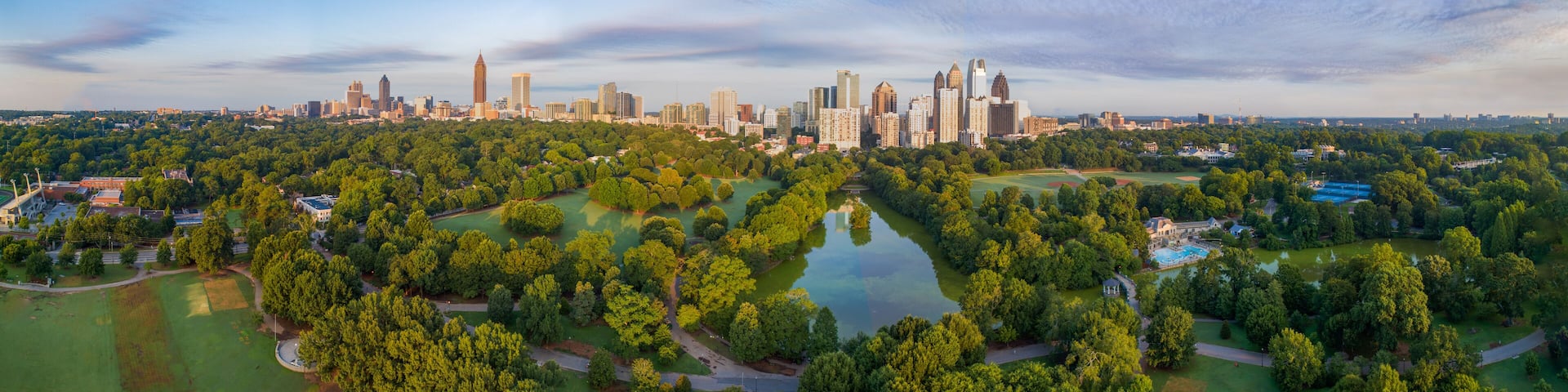 An aerial view of a city with a dense park area in the foreground and a skyline of high-rise buildings in the background.