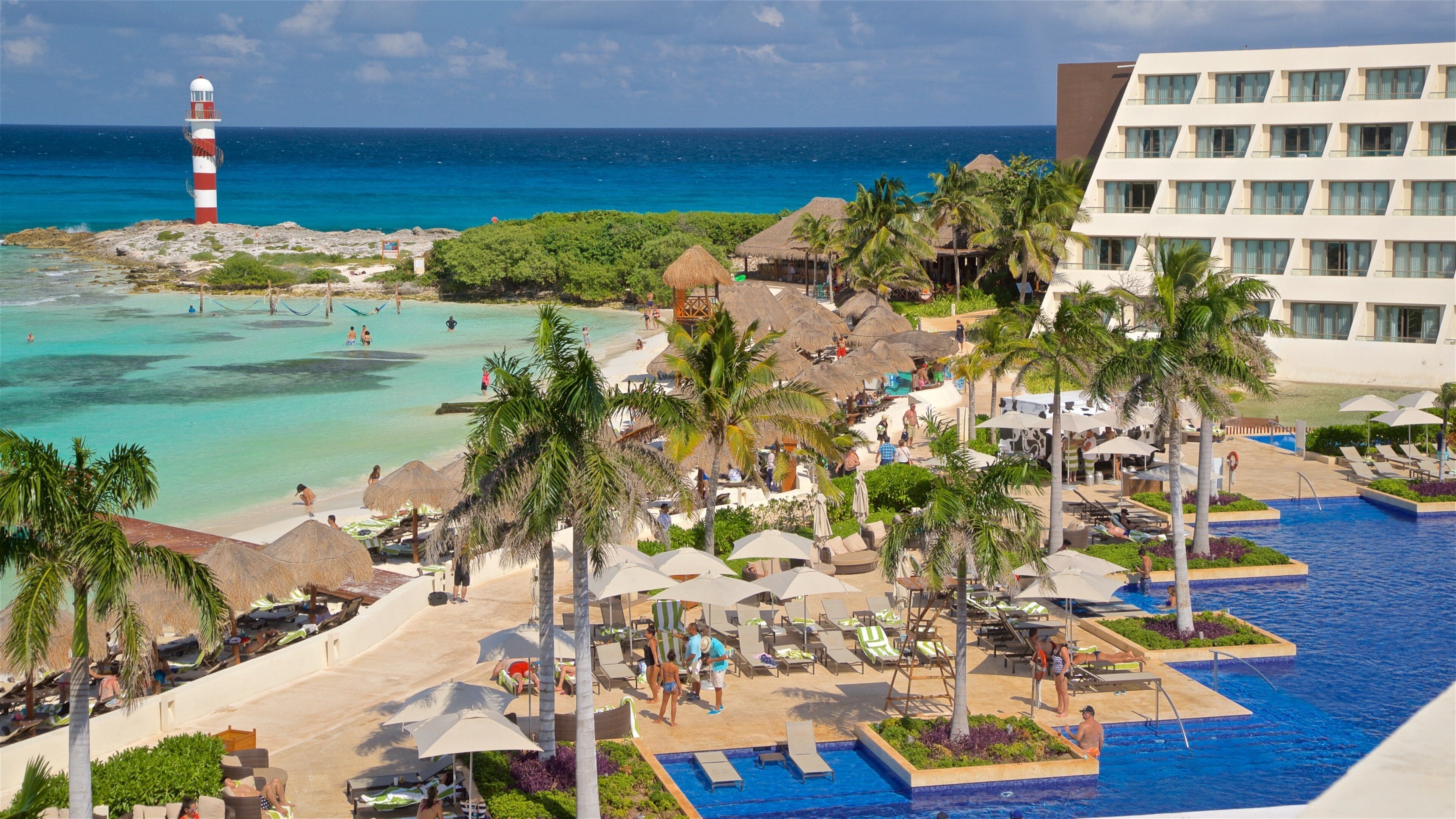A resort with a swimming pool, beach, palm trees, and a lighthouse.