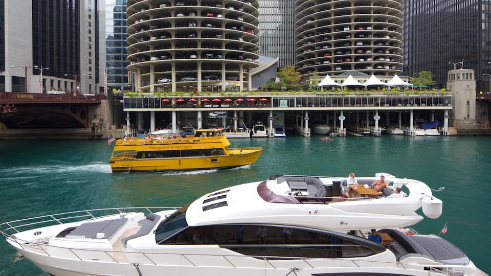 A river with a yellow boat and a white yacht. In the background, there are tall buildings and a bridge.