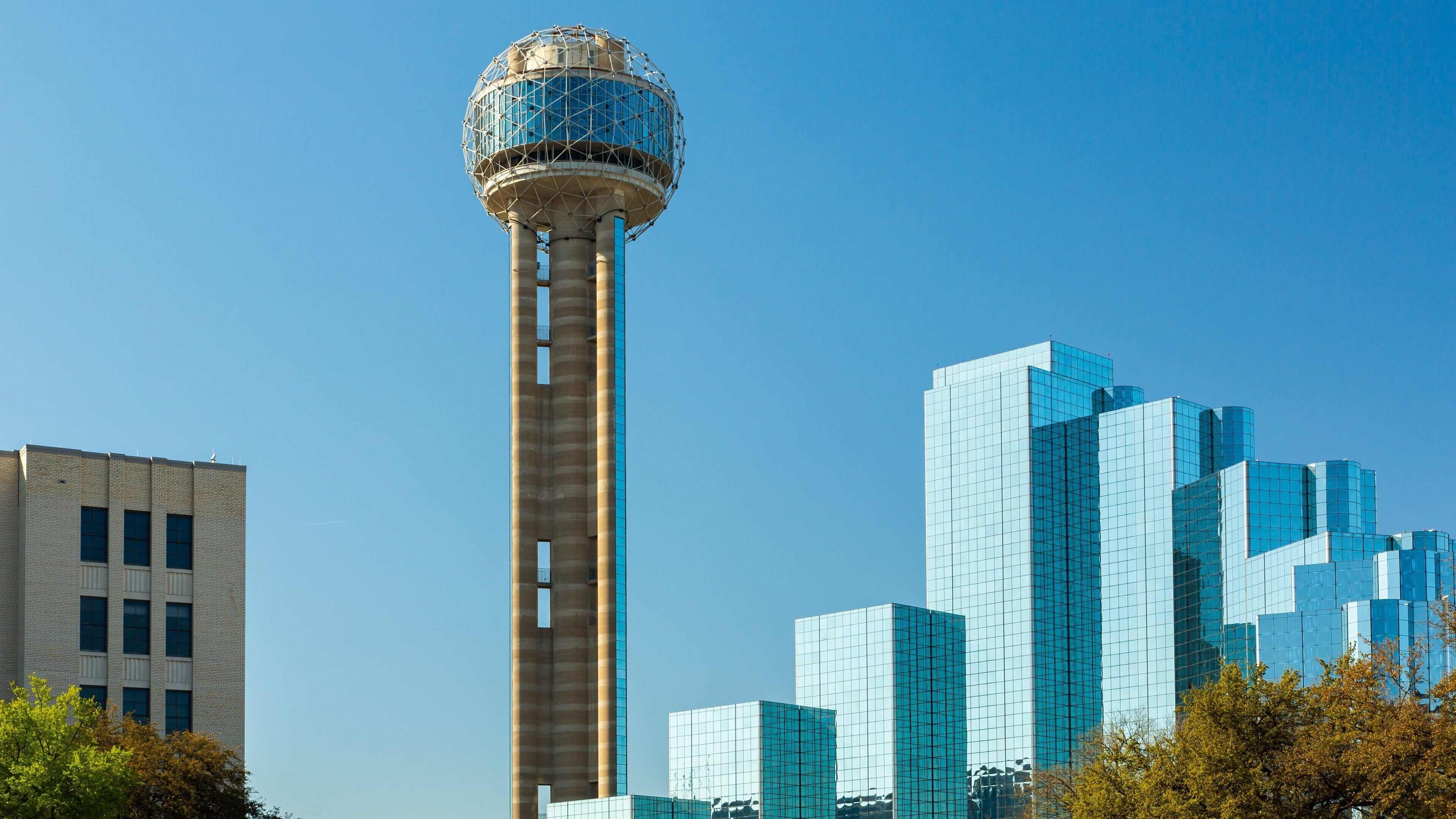 A water tower with a spherical top, surrounded by modern glass buildings.