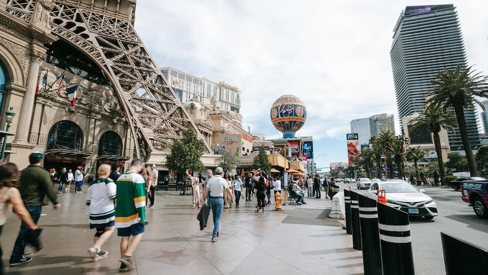 A busy urban street with historic architecture, including a large ornate building and a hot air balloon in the background.