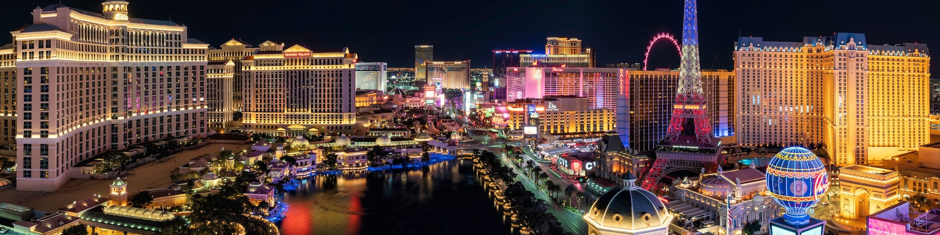 Vista noturna da Strip de Las Vegas, com hotéis iluminados, uma réplica da Torre Eiffel e o rio.