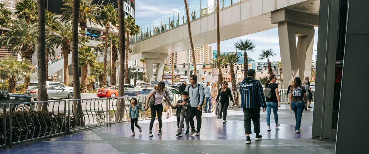 A busy urban street with palm trees, a pedestrian bridge, and a large advertisement for a restaurant.