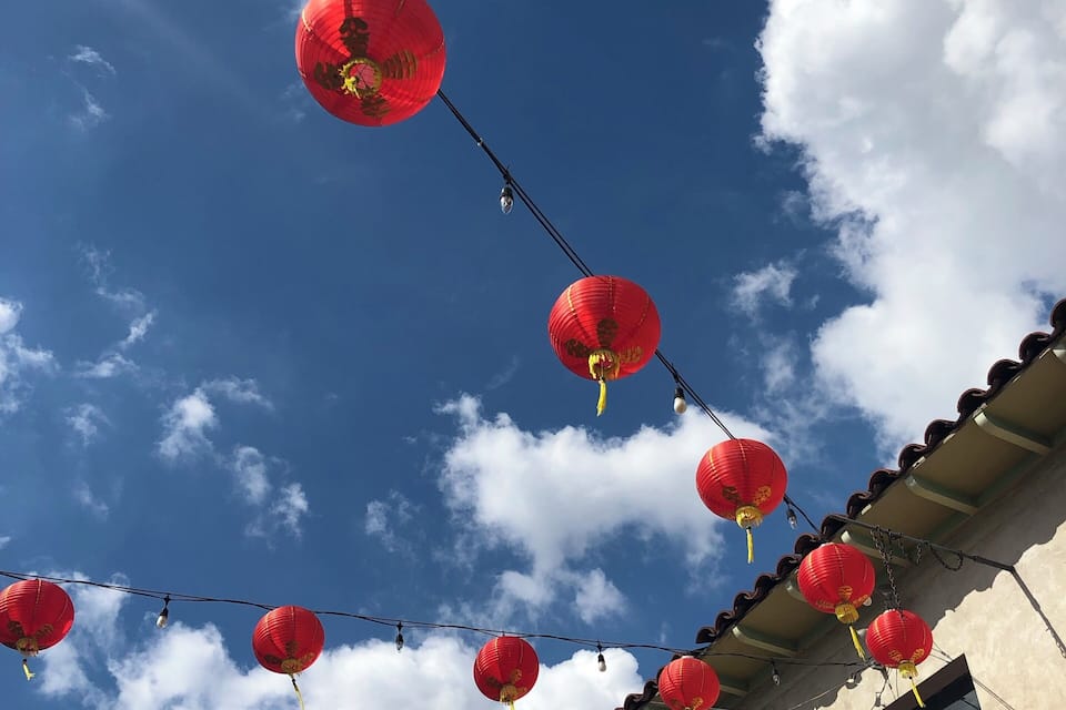 Un bâtiment décoré de lanternes rouges suspendues à des câbles, sur fond de ciel bleu et de nuages.