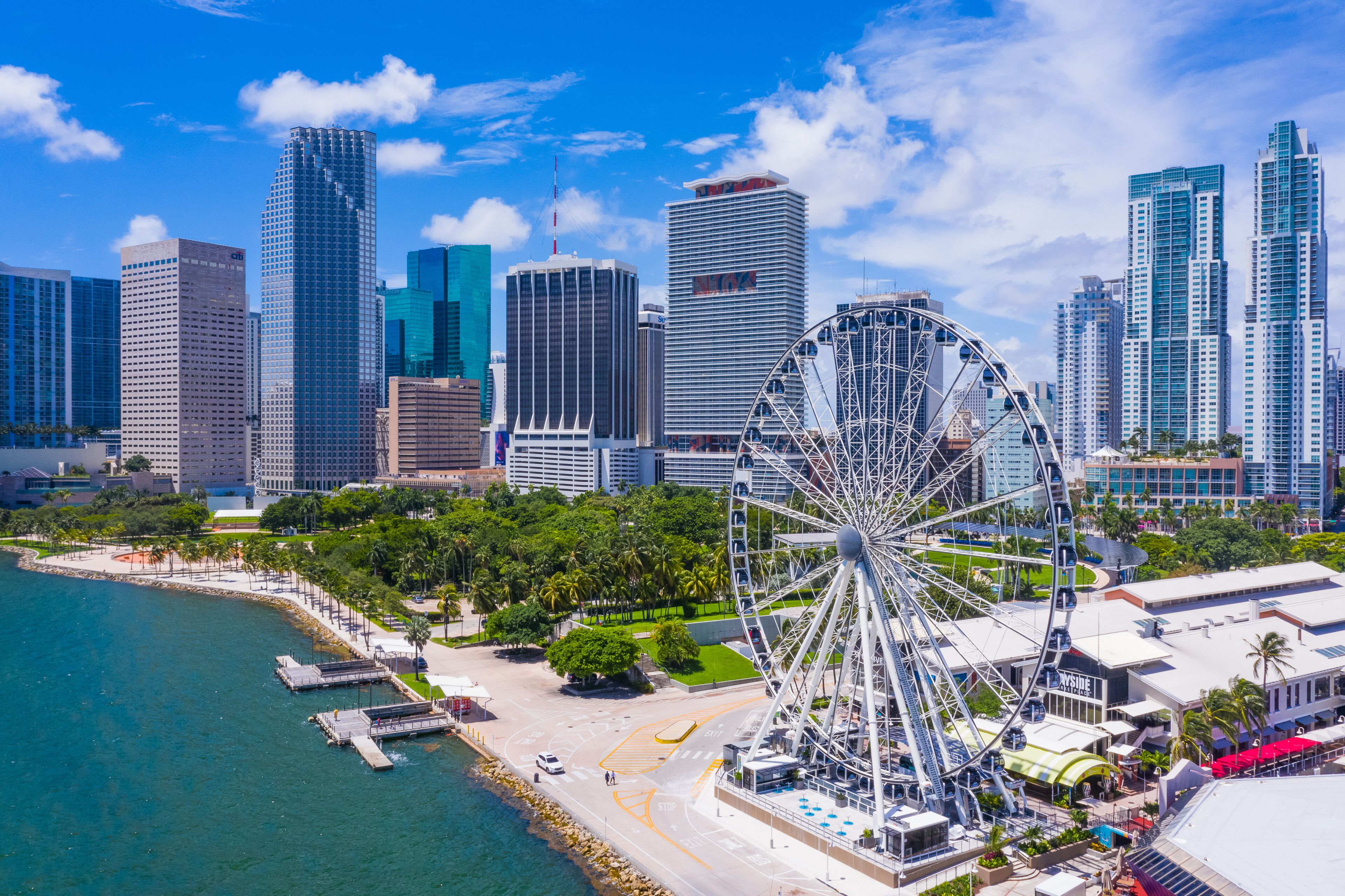 A coastal cityscape with a prominent Ferris wheel, high-rise buildings, and a marina.