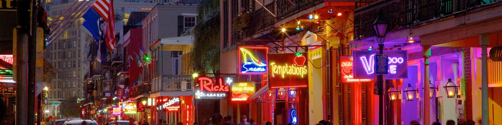 Uma rua movimentada, com lojas e restaurantes iluminados, incluindo Rick's e Temptations.