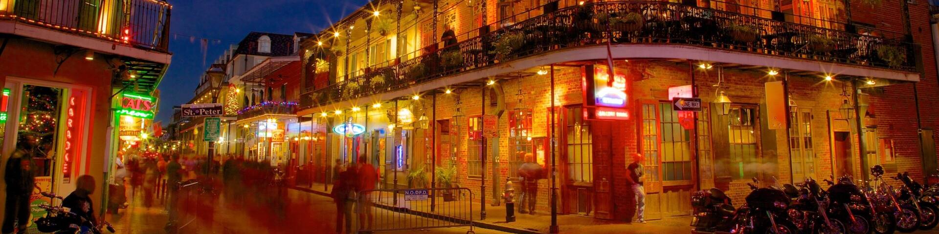 A brightly lit historic building with balconies and outdoor seating, surrounded by other buildings and parked motorcycles.