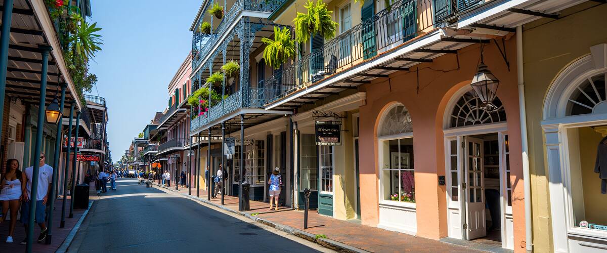A street lined with colorful buildings, balconies with plants, and pedestrians.