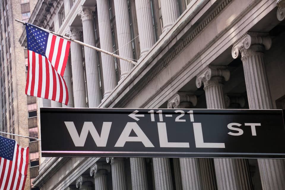 A street sign for Wall St. with American flags.