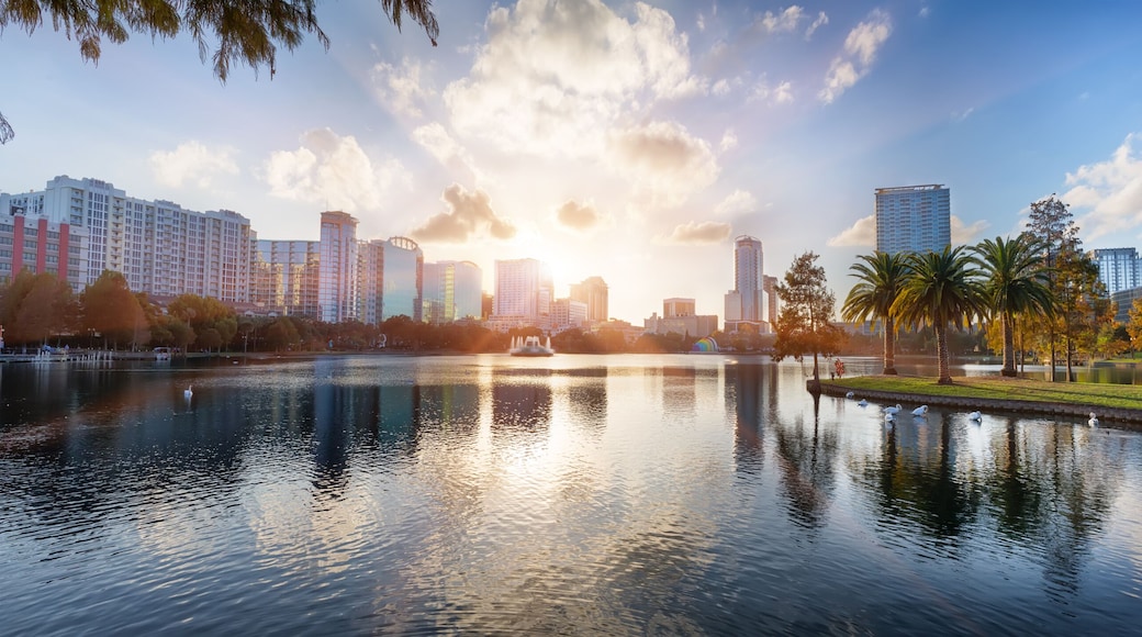 A cityscape with a body of water reflecting buildings, a park with trees, and a clear sky.