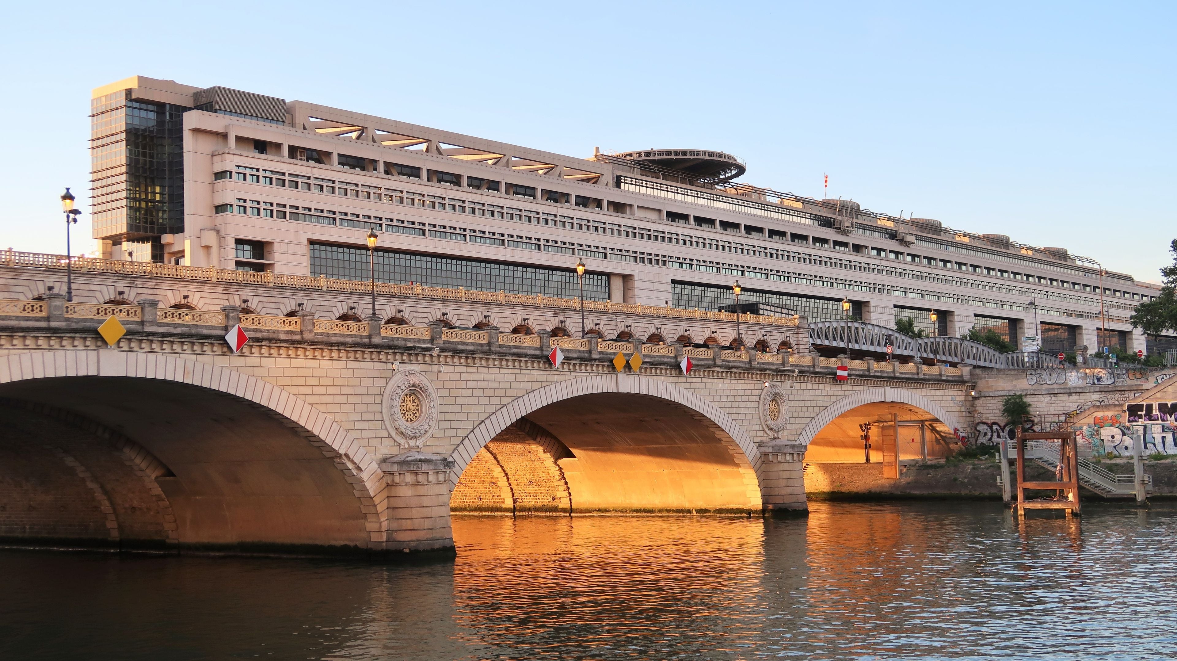 A bridge with arches over a river, a modern building with multiple floors, and decorative railings.