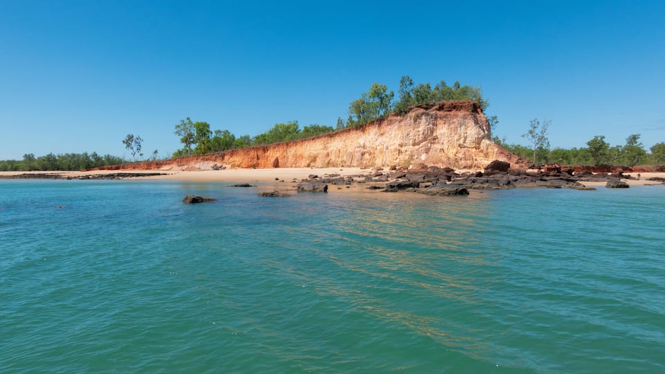 A coastal landscape with a prominent cliff, clear turquoise waters, and sparse vegetation.