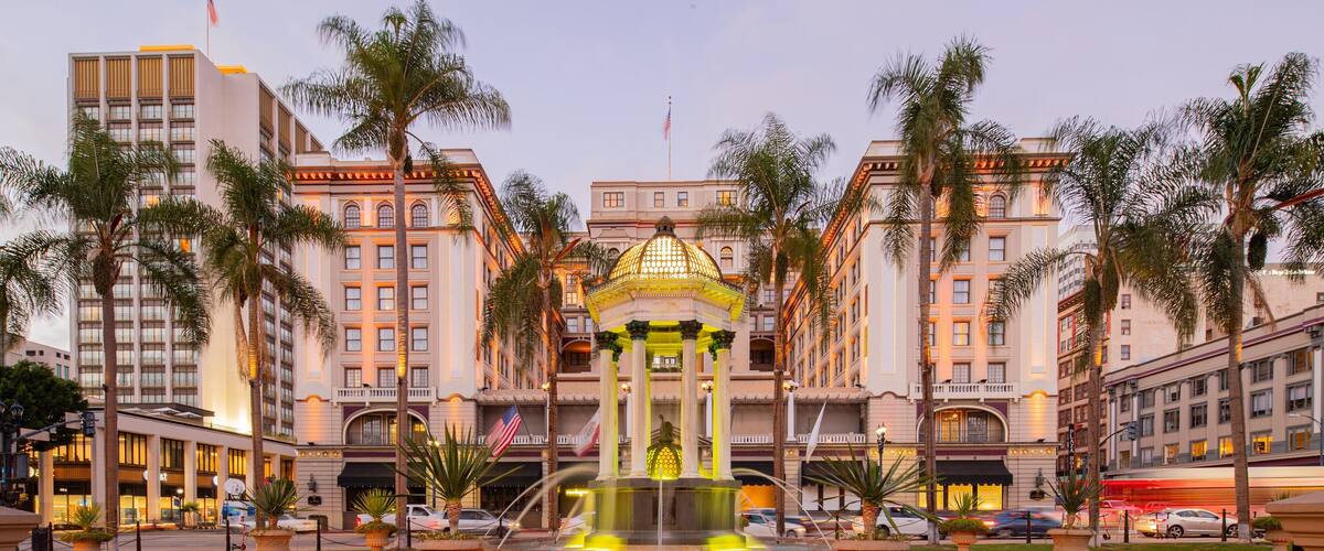 A grand building with a central fountain, palm trees, and a flag.