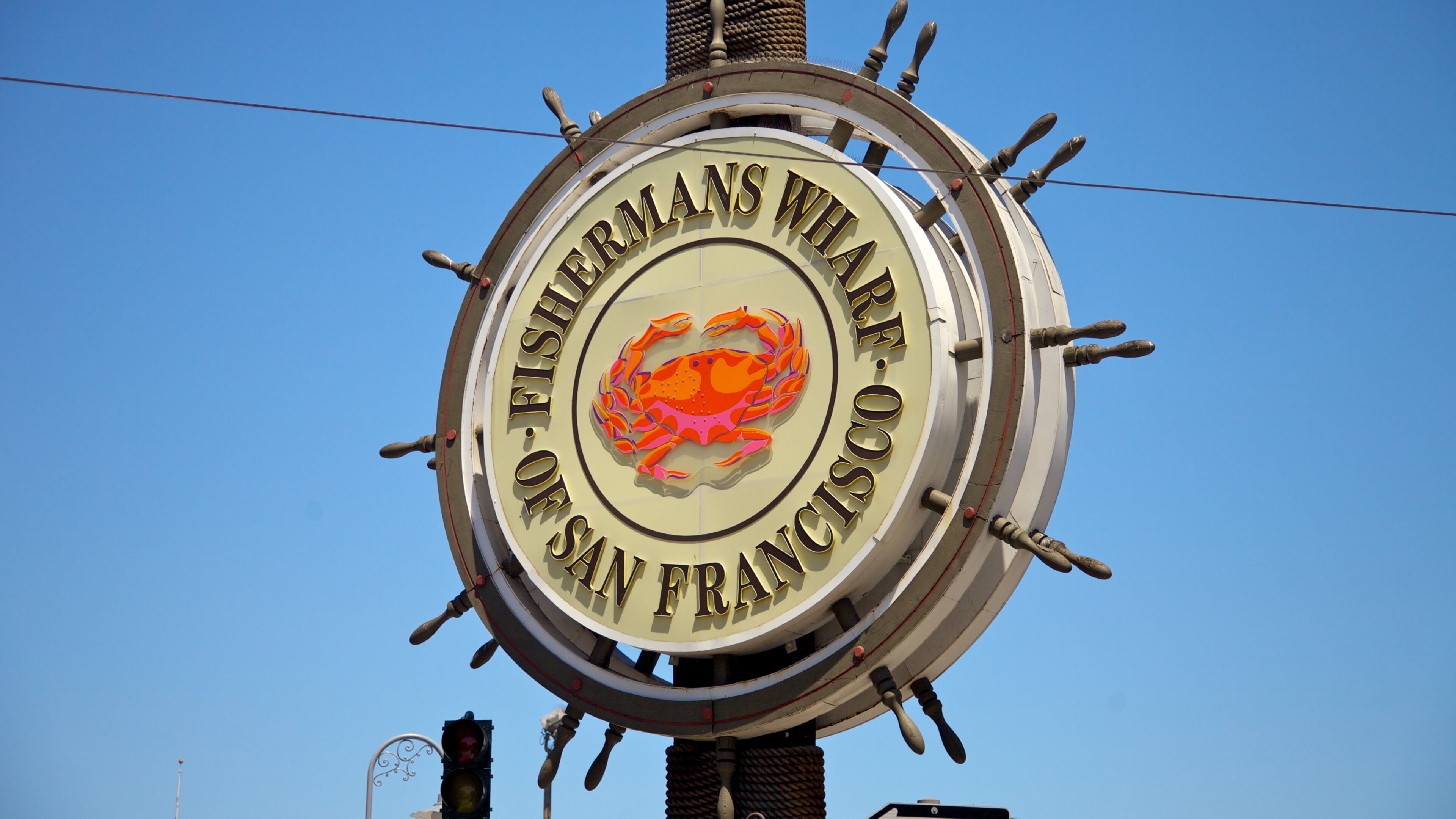 Un letrero circular con el emblema de un cangrejo y el texto 'FISHERMANS WHARF SAN FRANCISCO'.