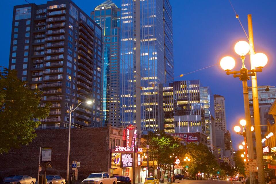 Een stadsgezicht in de schemering met verlichte gebouwen, straatverlichting en een neonbord voor 'Showgirls'.
