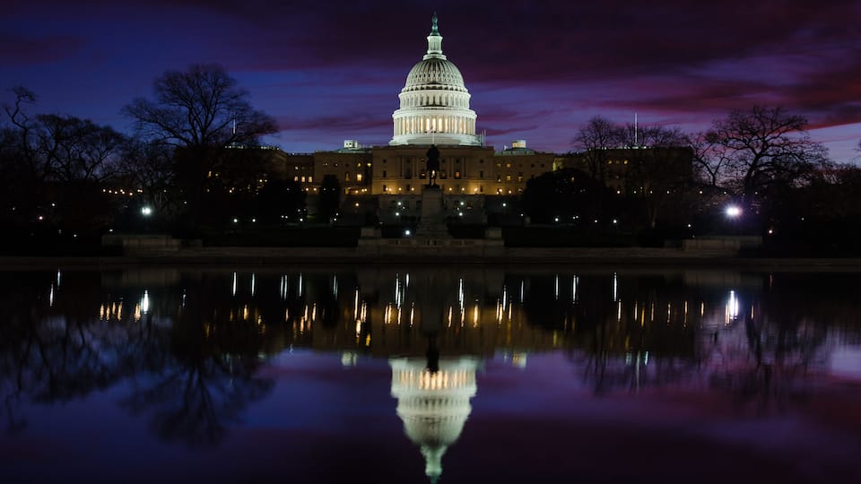 The Capitol building at dusk with its reflection in a body of water.