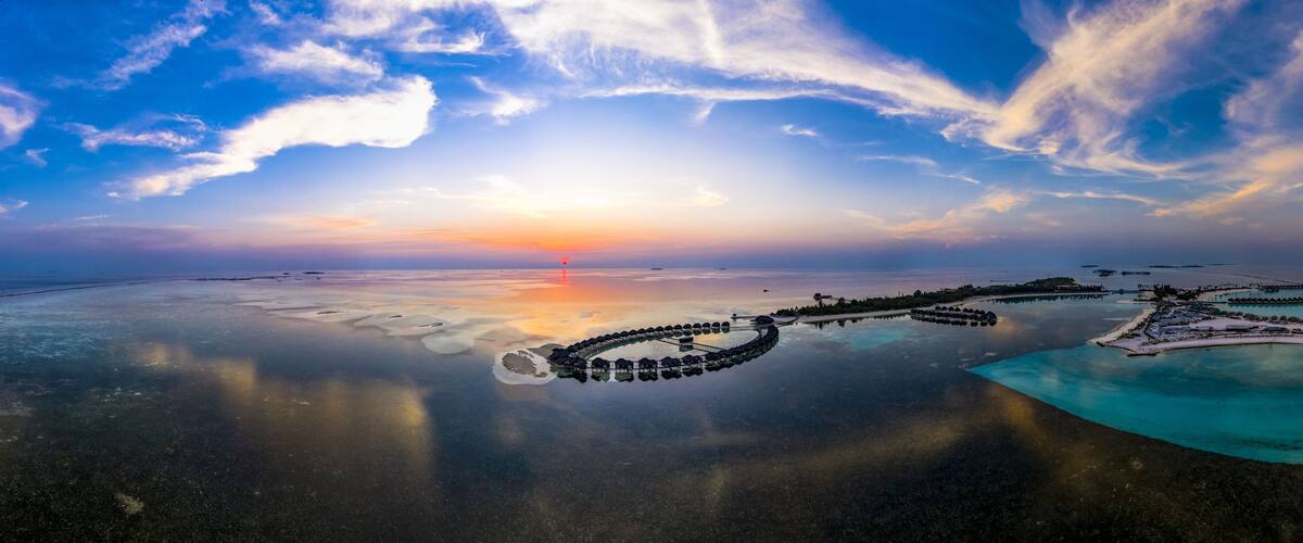 A tropical resort with overwater bungalows, a clear sky, and a sunset.