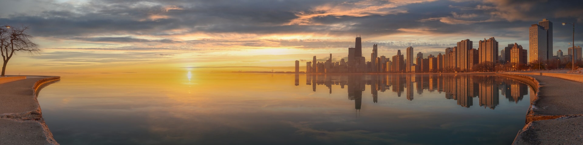 A city skyline reflected in a calm body of water during sunset.