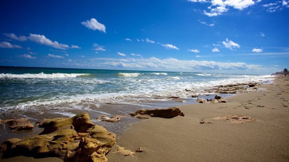 A sandy beach with waves crashing onto the shore and scattered rocks.