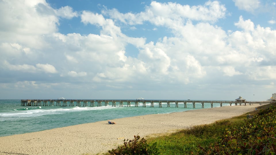 A beach with a wooden pier extending into the ocean, a sandy shore, and a partly cloudy sky.