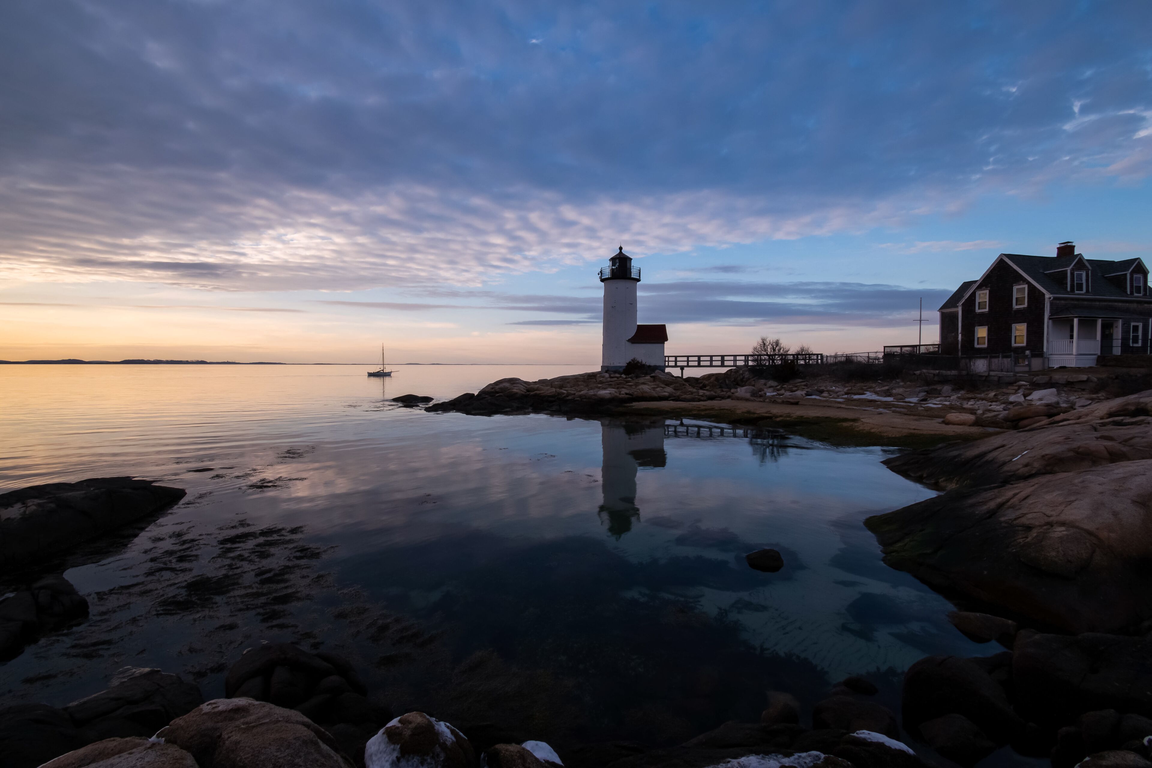 A lighthouse, a wooden house, and a calm body of water at dusk.