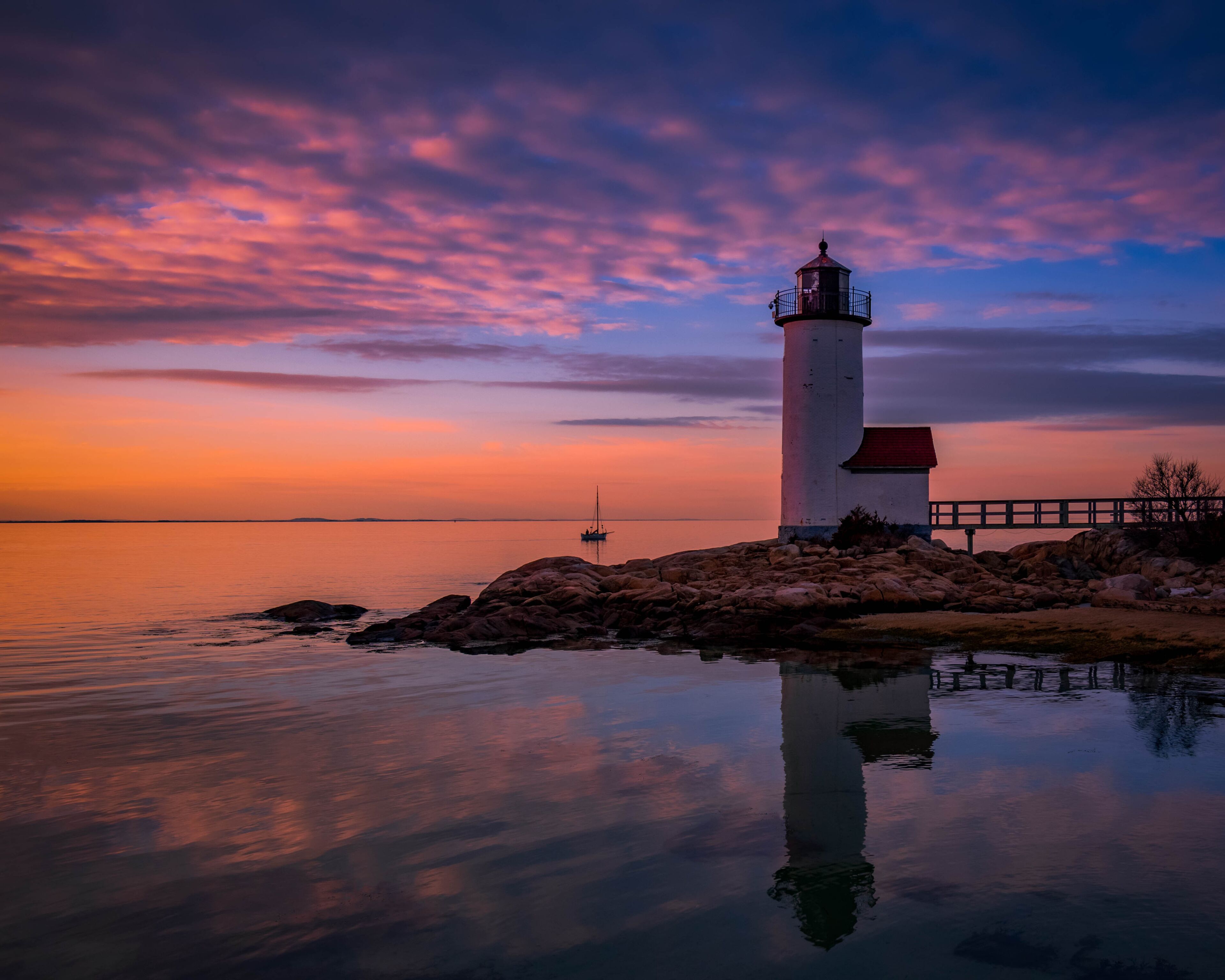 Um farol sobre um afloramento rochoso, com mar calmo e céu ao pôr do sol.