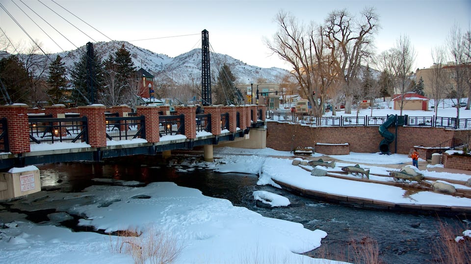 Un puente cubierto de nieve sobre un río, con montañas al fondo.