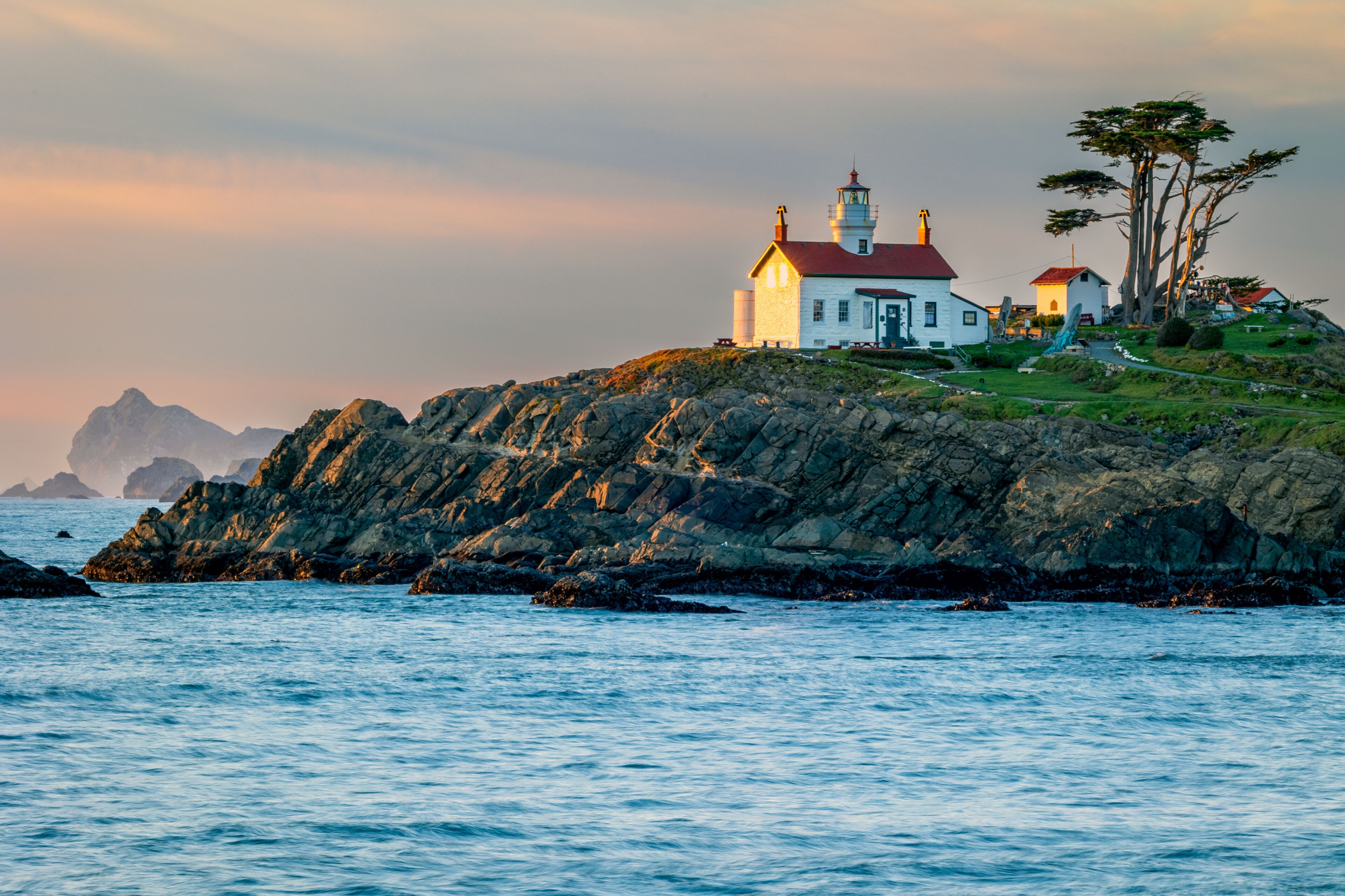 A coastal lighthouse, rocky shoreline, and distant mountains.