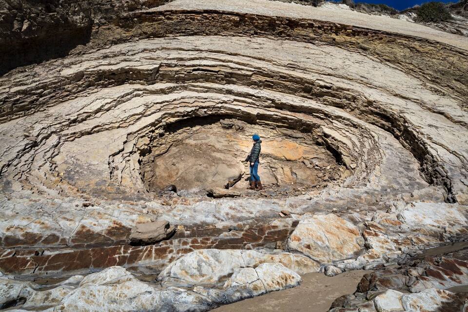A person standing in a large rock formation with layered sedimentary rock.