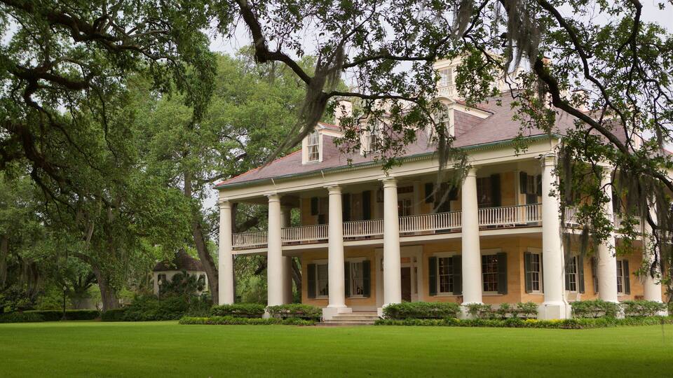 A large, historic house with a porch and columns, surrounded by lush greenery.