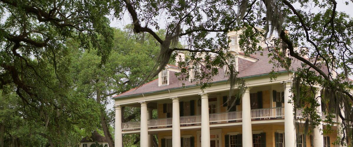 A large, historic house with a porch and columns, surrounded by lush greenery.