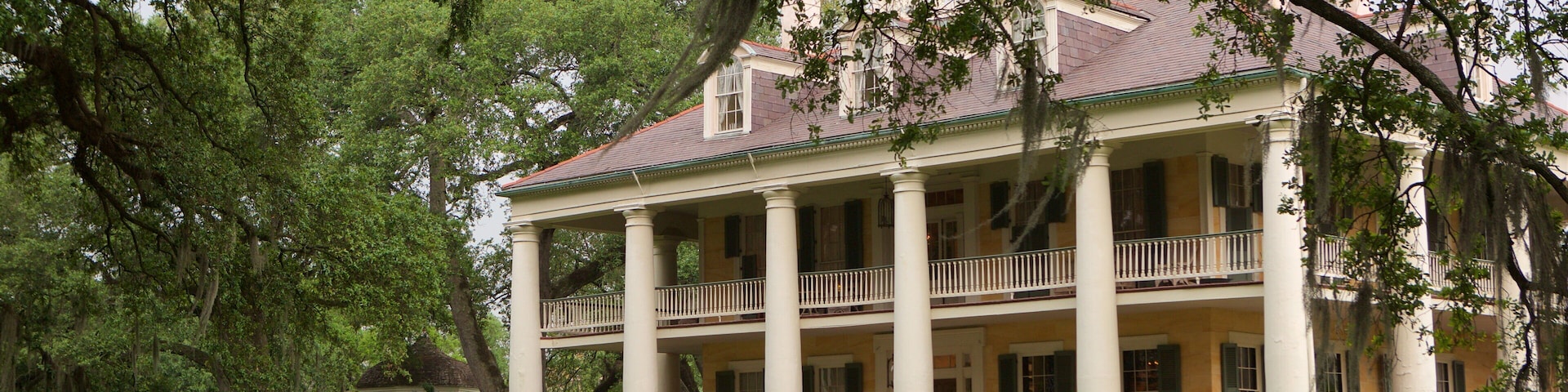 A large, historic house with a porch and columns, surrounded by lush greenery.