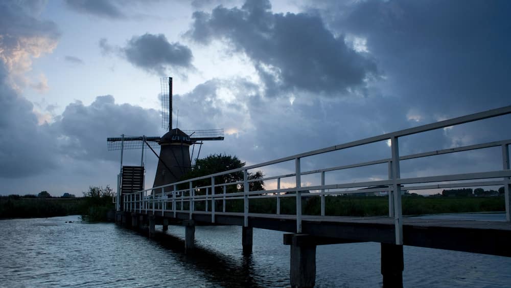 A windmill on a bridge over water, with a cloudy sky.