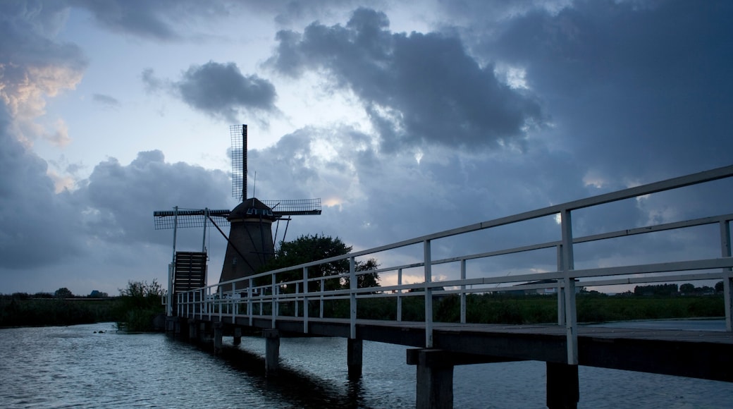 A windmill on a bridge over water, with a cloudy sky.