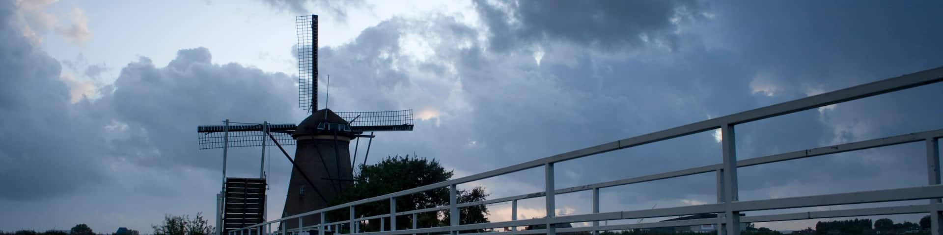 A windmill on a bridge over water, with a cloudy sky.