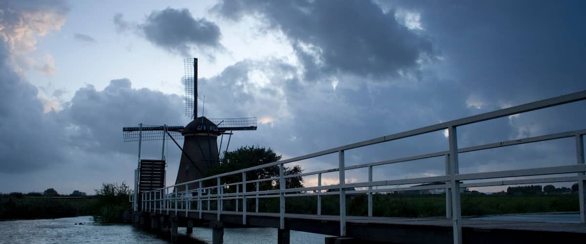 A windmill on a bridge over water, with a cloudy sky.