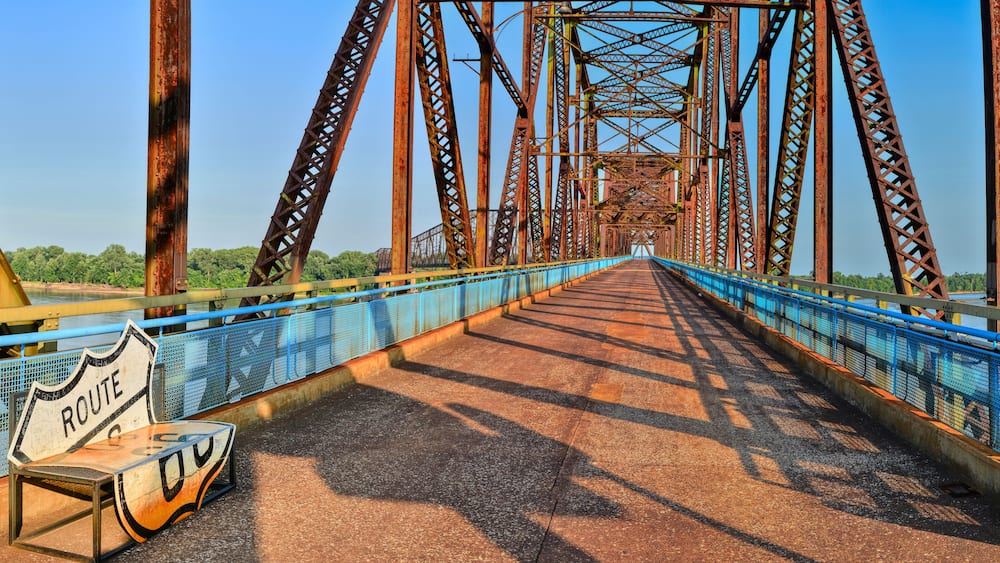 Eine große, verrostete Metallbrücke mit blauen Geländern und einem 'Route 66' Schild auf der linken Seite.
