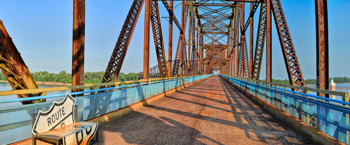 A large, rusted metal bridge with blue railings and a 'Route 66' sign on the left.