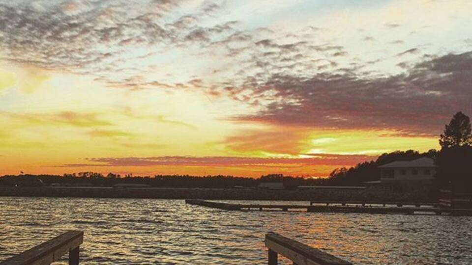 A wooden pier extending over calm water at sunset with a colorful sky.