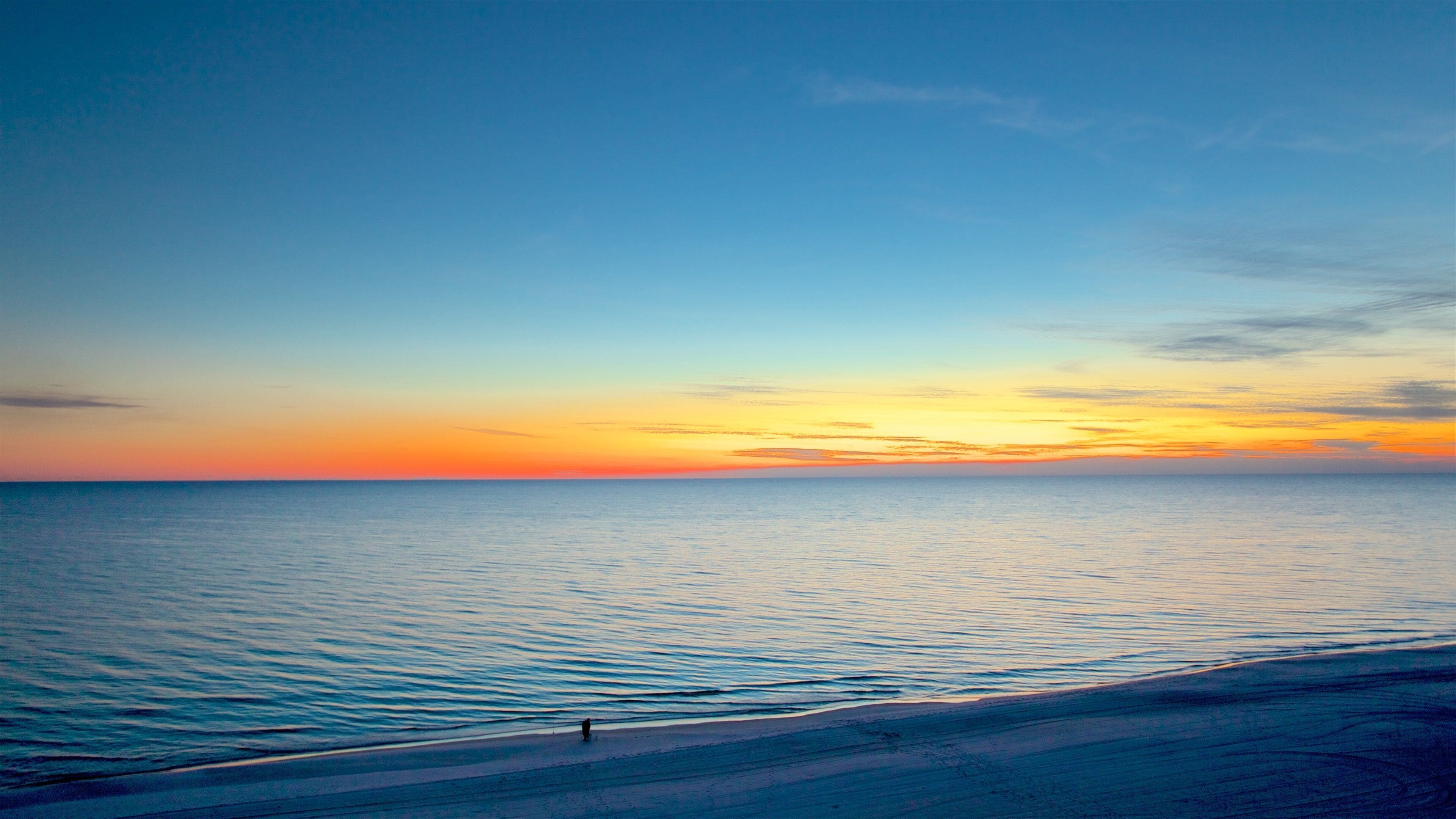 A beach at sunset with calm waters and a clear sky.