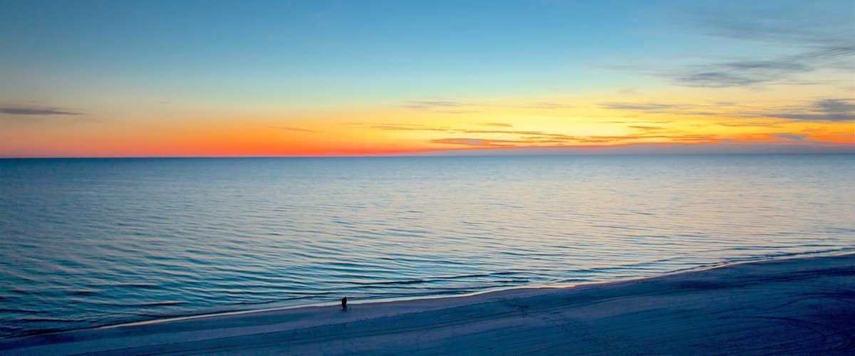 A beach at sunset with calm waters and a clear sky.