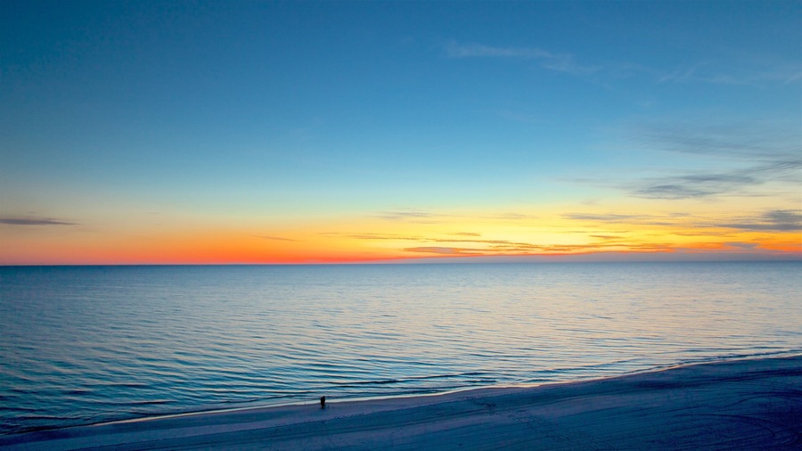 A beach at sunset with calm waters and a clear sky.