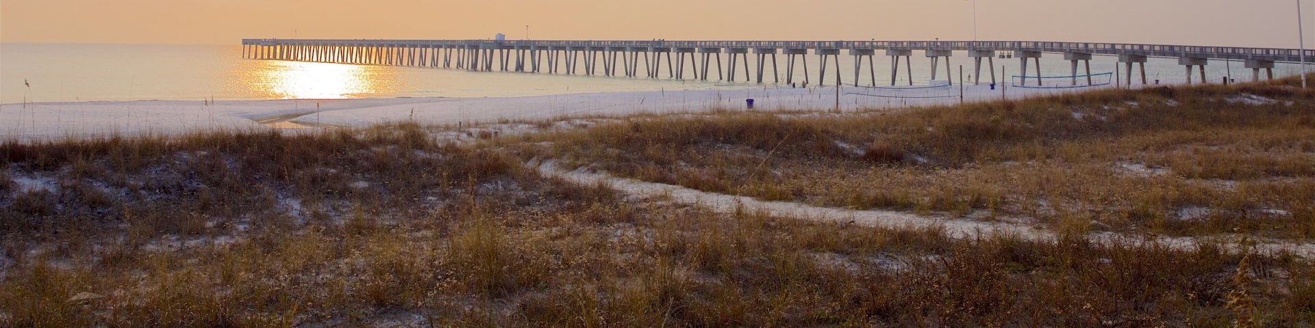 A beach with a pier extending into the water during sunset.