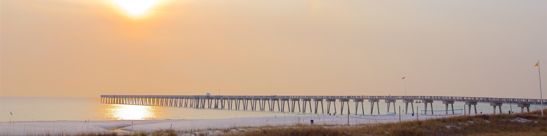 Una playa con un muelle que se adentra en el agua al atardecer.
