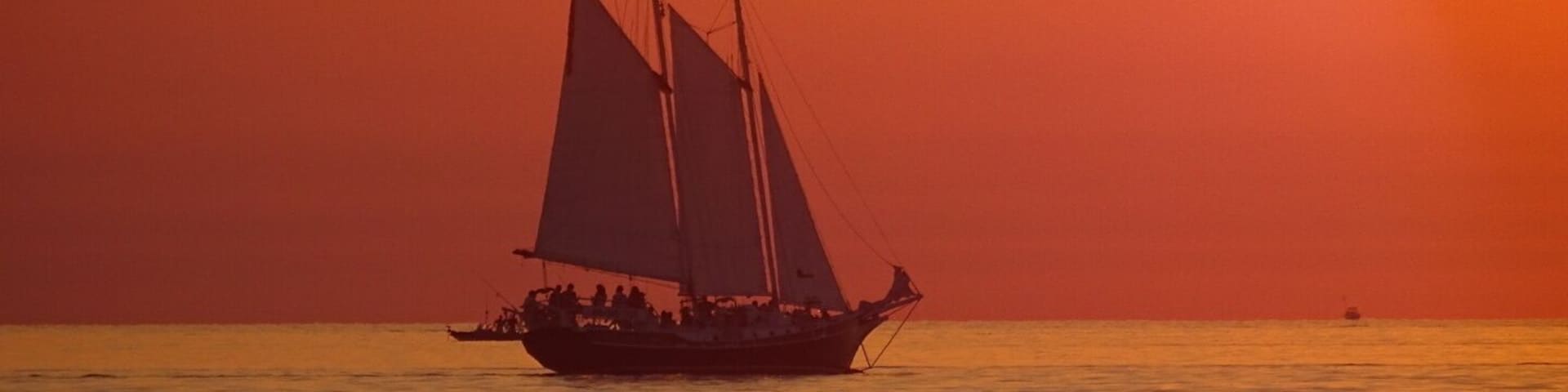 A sailboat with multiple sails on a calm sea during sunset.
