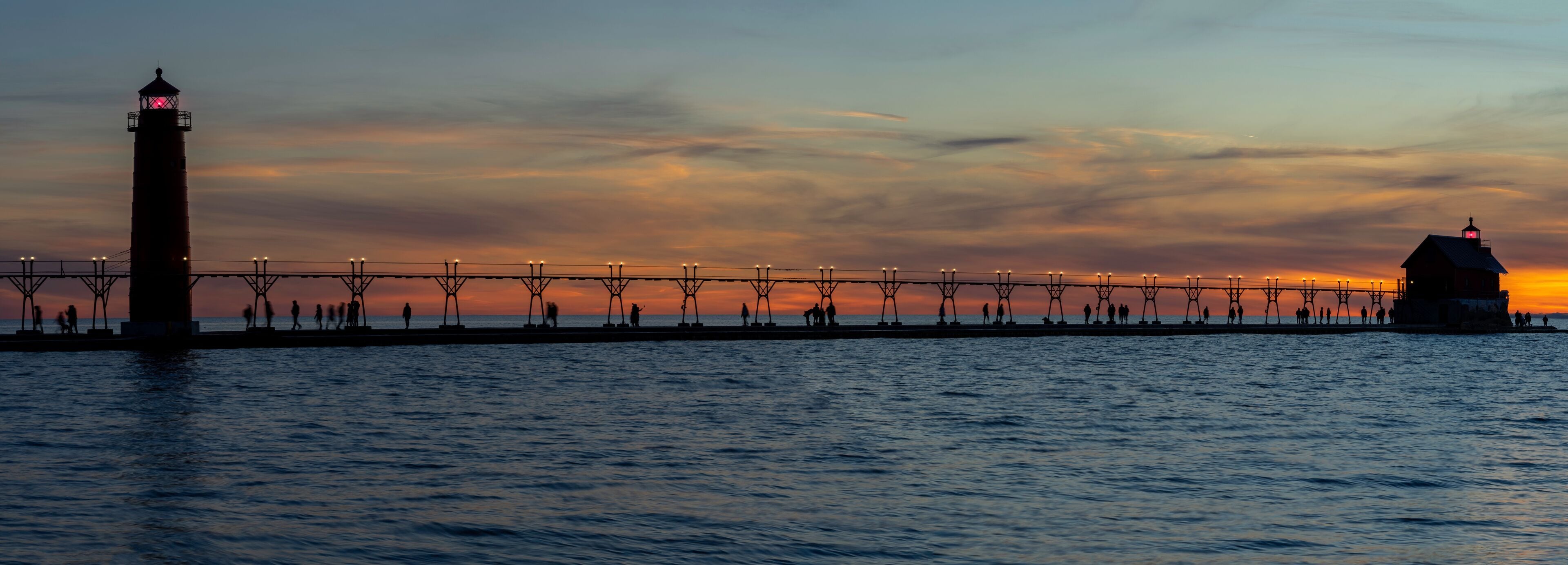 Grand Haven Lighthouse Michigan on Lake Michigan at sunset during the winter with beautiful colors and the structures and people silhouetted.  Hot from North Pier.