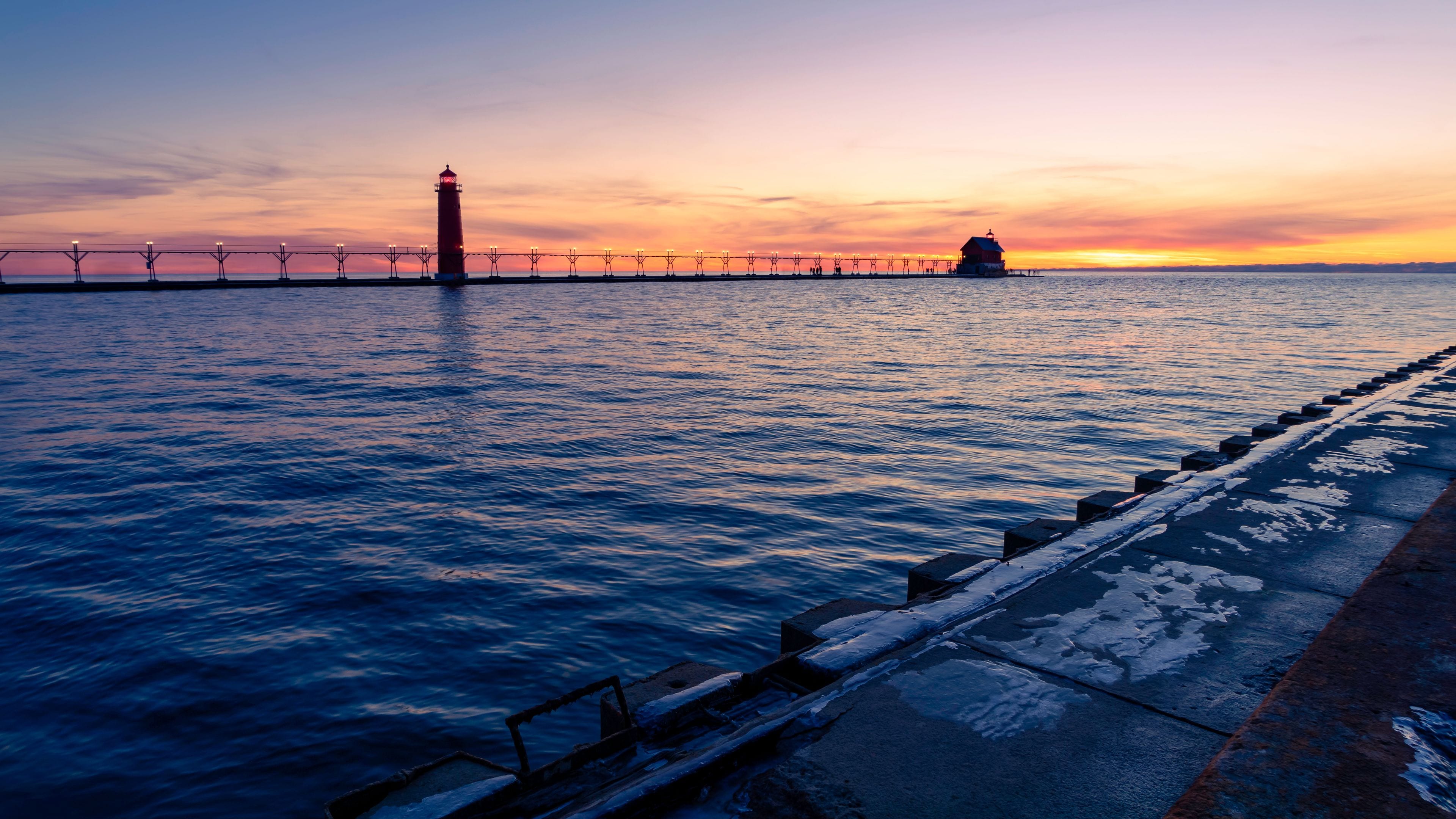 A coastal sunset with a lighthouse and pier extending into the water.