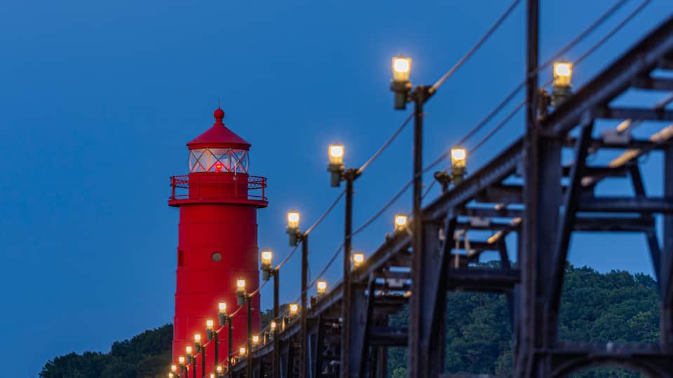 A red lighthouse with a glass lantern room, surrounded by a metal structure with lights.