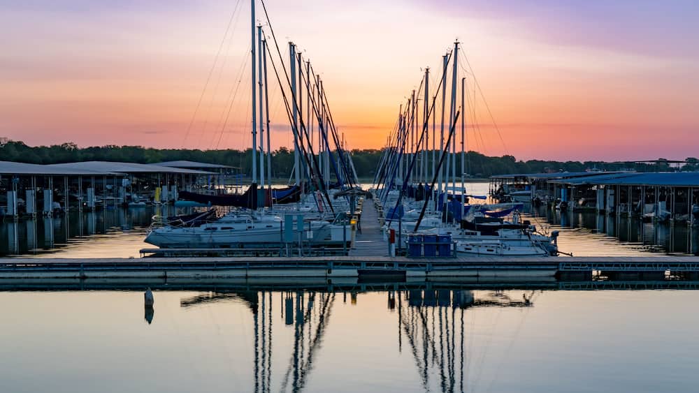 A marina with multiple sailboats docked at calm water during sunset.